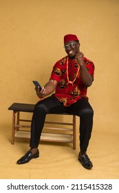 Igbo Traditionally Dressed Business Man Sitting Down and Staring at Phone and Smiling