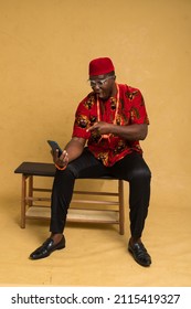 Igbo Traditionally Dressed Business Man Sitting Down and Staring at Phone and pointing