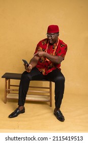 Igbo Traditionally Dressed Business Man Sitting Down and Staring at Phone and Pointing