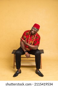 Igbo Traditionally Dressed Business Man Sitting Down and Display Imaginary Product and Look Forward