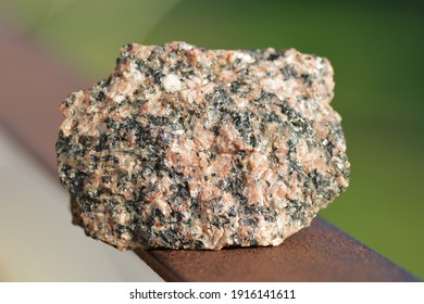 Igneous Rock: A Loose Raw Piece Of Granite Stone Specimen, Rough Chipped Irregular Shape, Brown Green Natural Backgroung On Bright Day Light Sharp Textured Crystal Elements Makro. Geology Theme.