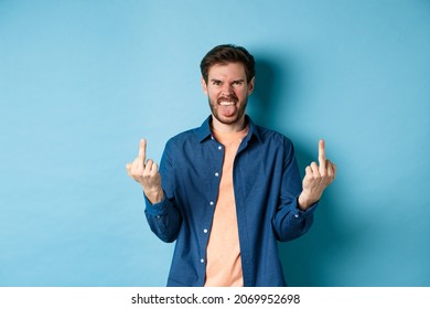 Ignorant And Rude Guy Showing Middle Finger And Smiling, Say Fuck You, Standing On Blue Background