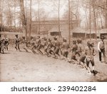 Igorot men from the Philippines dance in a semi-circle. The huts in the background are part of the Louisiana Purchase Exposition. 1904.