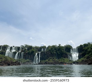 Iguazu Falls scenic view with powerful waterfalls, lush greenery, mist, and flowing river under cloudy sky. Iguazu National Park, Brazil Argentina border. - Powered by Shutterstock