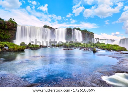 Iguazu waterfalls in Argentina, view from Devil's Mouth. Panoramic view of many majestic powerful water cascades with mist and reflection of blue sky with clouds. Panoramic image of Iguazu valley.