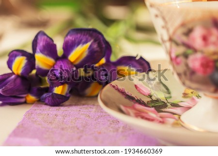 IIris flowers and traditional porcelain tea cup with saucer with floral paining . Spring, summer  background. Selective focus, side view