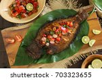 Ikan Bakar Dabu-Dabu. Popular dish of grilled fish with fresh and spicy tomato salsa from Manado. Served on a wooden block lined with broad leaves.