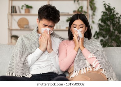 Ill Asian Couple Having Cold, Blowing Nose Sneezing In Paper Tissue Sitting On Couch At Home Feeling Unwell. Rhinitis And Seasonal Allergy, Flu Illness. Family On Sick Leave Self-Isolation Concept - Powered by Shutterstock