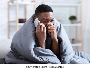 Ill Black Man Calling Doctor Having Runny Nose Suffering From Cold And Rhinitis Sitting On Sofa At Home. Sick African Guy Talking On Phone Feeling Unwell. Symptoms. Influenza Symptoms