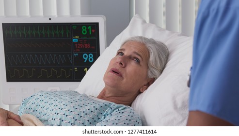 Ill Elderly Woman Resting In Hospital Bed Hooked Up To ECG Monitor