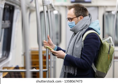 Ill man in glasses feeling sick, wearing protective mask against transmissible infectious diseases and as protection against the flu in public transport/subway, 
using and looking at smartphone - Powered by Shutterstock