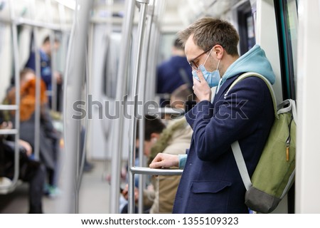 Ill man in glasses feeling sick, coughing, wearing protective mask against transmissible infectious diseases and as protection against the flu in public transport. New coronavirus 2019-nCoV from China