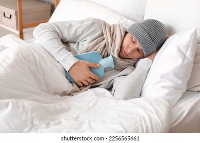Ill man lying with hot water bottle in bedroom - Powered by Shutterstock