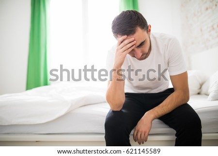 Ill man sitting on his bed with his head on his hand