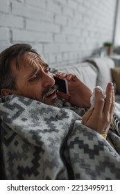 Ill Man Wrapped In Warm Blanket Holding Paper Napkin And Talking On Mobile Phone