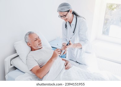 Ill mature man signing important documents in hospital ward bed. Medical insurance concept. Senior man looking through the documents for hospitalization - Powered by Shutterstock