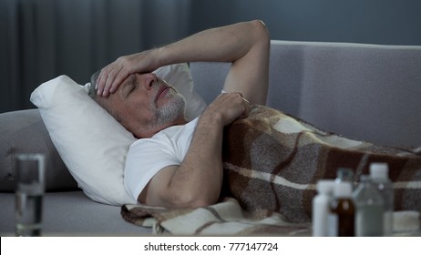 Ill senior male lying in bed and suffering from terrible headache, disease