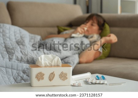 Ill sick middle aged woman sneezing blowing running nose holding tissue sit on bed, upset mature lady caught cold got flu influenza grippe symptoms taking medications at home alone