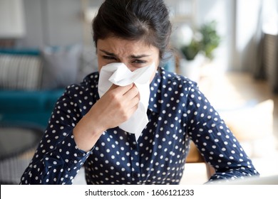 Ill upset indian girl holding paper tissue blowing running nose sneezing in handkerchief got flu fever caught cold influenza sit at home, flue sinus virus disease symptom concept, face close up view