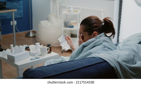 Ill Woman Reading Package Leaflet For Information About Medication And Healing Treatment. Person With Virus Symptoms Holding Medical Paper While Having Pills And Capsules On Table.