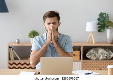 Ill At Work Young Man Got Flu Allergy Sneezing Blowing Wiping Running Nose In Tissue, Allergic Guy Caught Cold At Job Sitting At Home Office Workplace Having Respiratory Disease, Sick Leave Concept