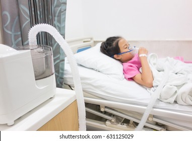 Ill Young Asian Girl Sleeping On Bed In Hospital. Sick Kid With Medical Ultrasonic Inhaler, Nebulizer, Nebular With Mask. Respiratory Medicine. Asthma Breathing Treatment. Asthmatic Health Equipment. 