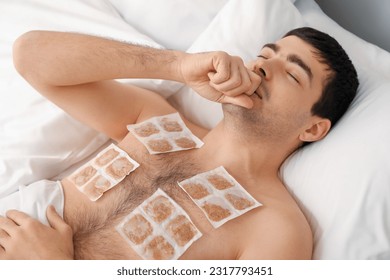Ill young man with mustard plasters on his chest lying in bedroom