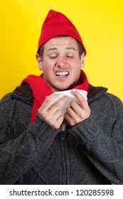 Ill young man with red nose, scarf and cap sneezing into handkerchief