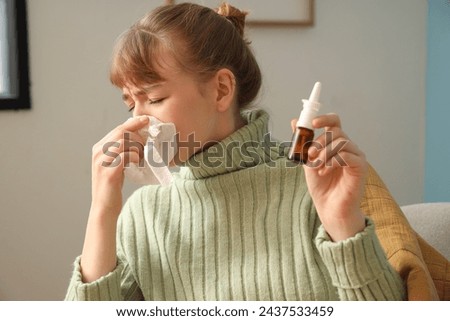 Ill young woman with nasal drops and tissue sneezing at home, closeup
