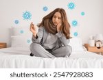 Ill young woman with thermometer sitting on bed