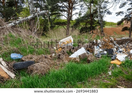 Illegal dumping of assorted trash, logs, and general debris mars a natural grassy field near forest trees. A clear depiction of environmental neglect