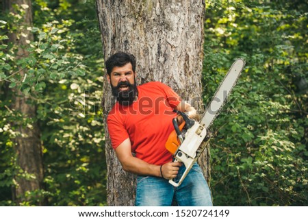 Illegal logging continues today. Lumberjack in the woods with chainsaw axe. Lumberjack on serious face carries chainsaw. Woodcutter with chainsaw on sawmill