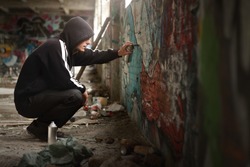 Illegal Young Man Spraying Black Paint On A Graffiti Wall. (room For Text)