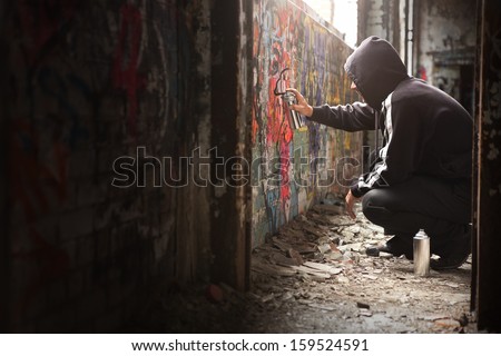 Illegal Young man Spraying black paint on a Graffiti wall. (room for text)