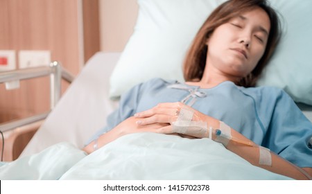 illness asia patient women and hospital concept - hand with iv solution of illness asian patient women on bed sleeping in patient room alone of hospital with flare light effect and copy space