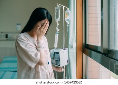 Illness Chinese Lady Patient Woman Standing By Bed Seeing Windows In Room Alone Of Hospital. Upset Young Girl Crying Covering Face With Hands Feeling Lonely. Sick Female With Intravenous Injection