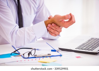Illness hand. Portrait of a businessman with a beard while working in his office, holding hand