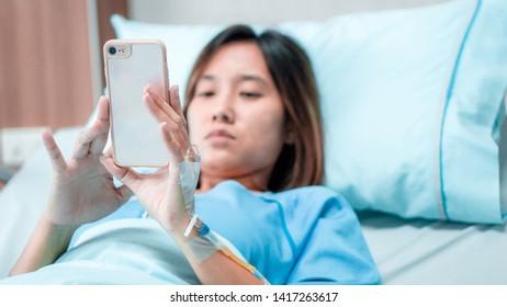 Illness Patient Women And Hospital Concept - Illness Asian Patient Women Using Mobile Phone For Checking Information On Social Media In Patient Room Of Hospital With Flare Light Effect And Copy Space