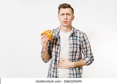 Illness Sad Young Man In Shirt Put Hand On Pain Abdomen, Stomach-ache, Standing And Holding Burger Isolated On White Background. Proper Nutrition Or American Classic Fast Food. Area With Copy Space