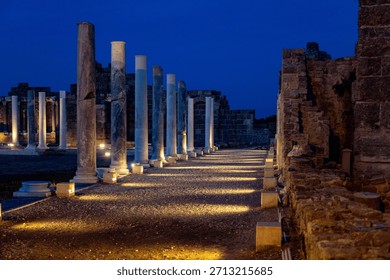Illuminated ancient columns create a dramatic linear perspective at the agora under a dark blue night sky. A journey into history. Side, Antalya, Turkey, Mediterranean.

