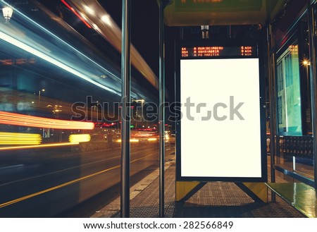 Illuminated blank billboard with copy space for your text message or content, advertising mock up banner of bus station, public information board with blurred vehicles in high speed in night city 