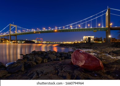 Illuminated bridge over a river with a red boulder in the foreground. Gothenburg, Sweden.
