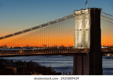 Illuminated Brooklyn Bridge at sunset and the Statue of Liberty with lighted torch in the distance. Close-up of historical New York City landmarks - Powered by Shutterstock