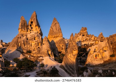Illuminated by the last rays of the setting sun fairy chimneys with the homes carved in a cliffs near Uchisar castle in Cappadocia, Turkey.