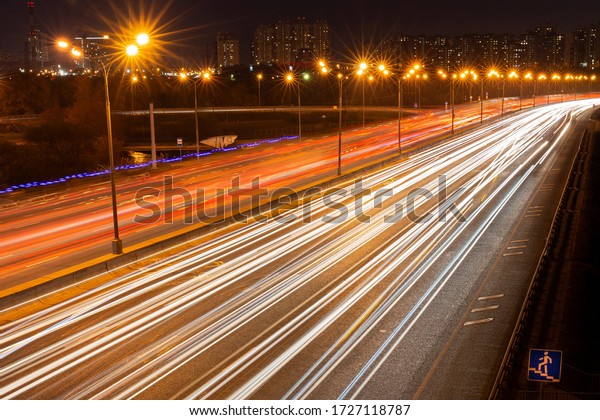 Illuminated by street\
lamps, the night road With the traces of passing cars \' headlights.\
Long-exposure\
photo.