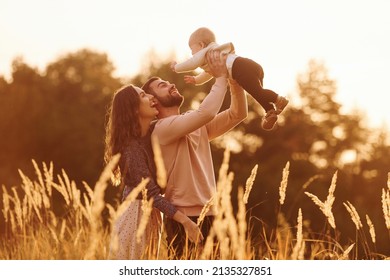 Illuminated By Sunlight. Happy Family Of Mother, Family And Little Baby Rests Outdoors. Beautiful Sunny Autumn Nature.