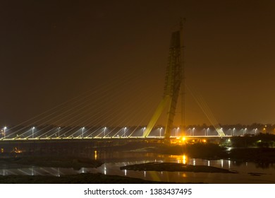 illuminated cable-stayed bridge under construction with a tower crane over the Yamuna River at night. Signature Bridge. Delhi India.