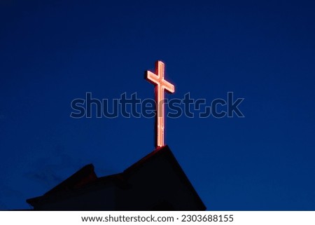 Illuminated cross on a church during blue hour. Christian cross with blue background against the sky. Worshipping concept.