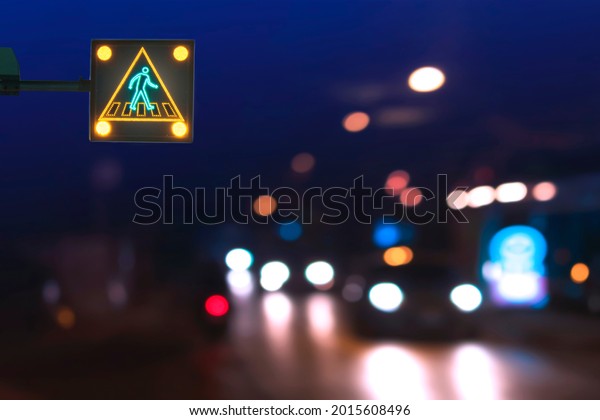 Illuminated electric traffic light\
pedestrian crossing sign with blurred night city street\
background