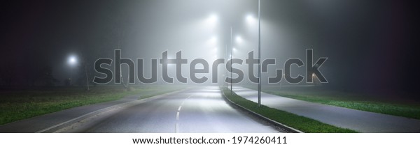 Illuminated empty asphalt road in a fog at\
night. Dark urban scene, cityscape. Industrial zone in Riga,\
Latvia. Dangerous driving, speed, freedom, concept\
image